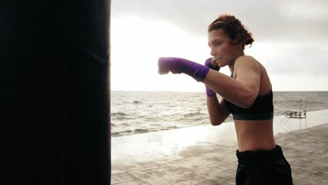 Close-Up-view-of-a-young-woman-training-with-the-boxing-bag-against-the-son.-Her-hands-are-wrapped-in-purple-boxing-tapes