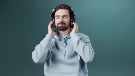 an attractive young man in a blue sweater is listening to music and nodding his head