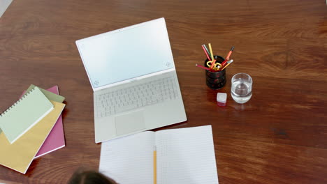 Overhead-of-biracial-girl-having-school-class-on-laptop-at-home,-copy-space-on-screen,-slow-motion