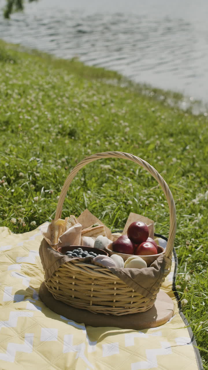 A picnic basket filled with food on a blanket by the lake