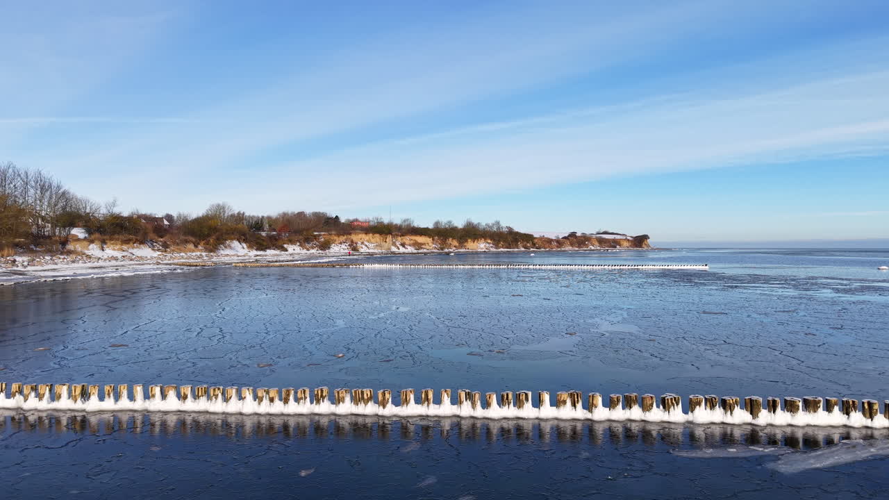 Vista aerea con drone della costa parzialmente ghiacciata del Mar Baltico durante l'inverno. L'immagine cattura superfici d'acqua ghiacciate, lastre di ghiaccio alla deriva e una costa innevata sotto un cielo azzurro e limpido.