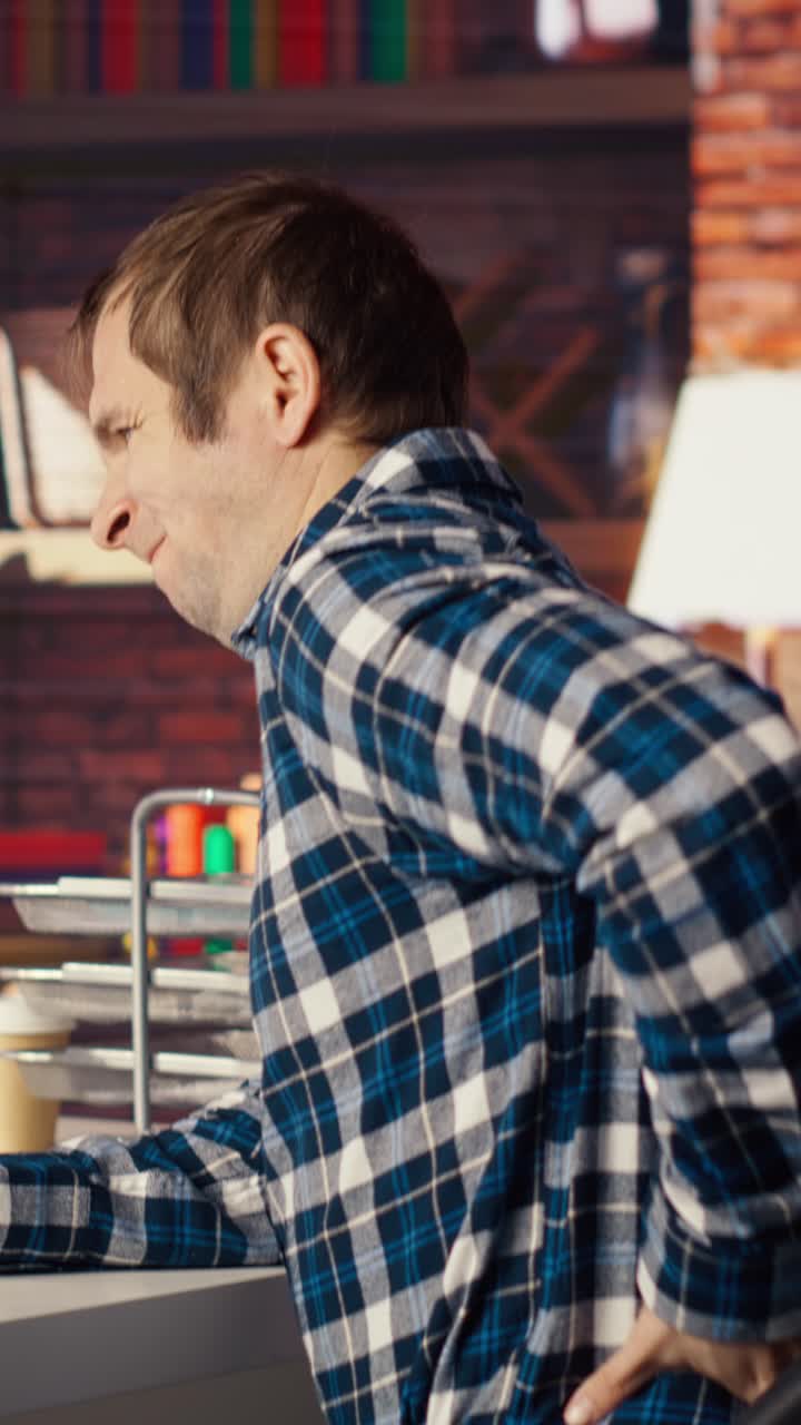 Vertical video Man at home stretching back while looking at UI on PC screen, feeling fatigued