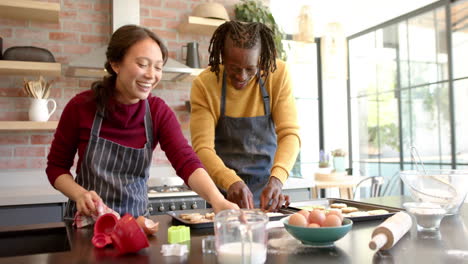 una pareja feliz y diversa en delantales horneando galletas de navidad en la cocina, en cámara lenta.