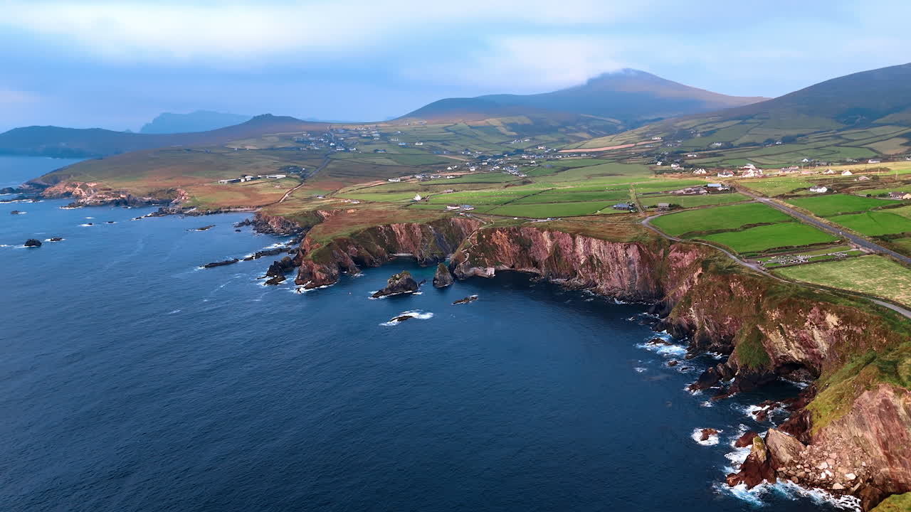 Mighty rocks at the shore of picturesque Ireland. The Atlantic Ocean at the coast with cottages scattered by the valley.
