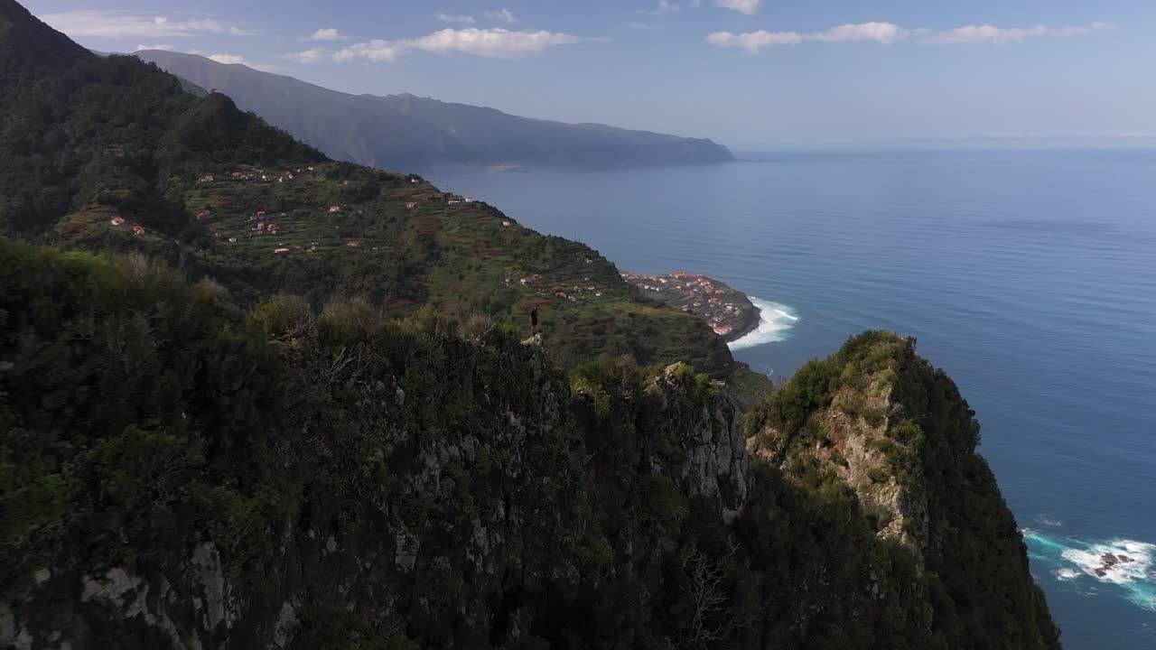 Un filmato con drone che vola all'indietro allontanandosi da un giovane uomo in piedi sul bordo di una scogliera in cima a una montagna a Madeira.