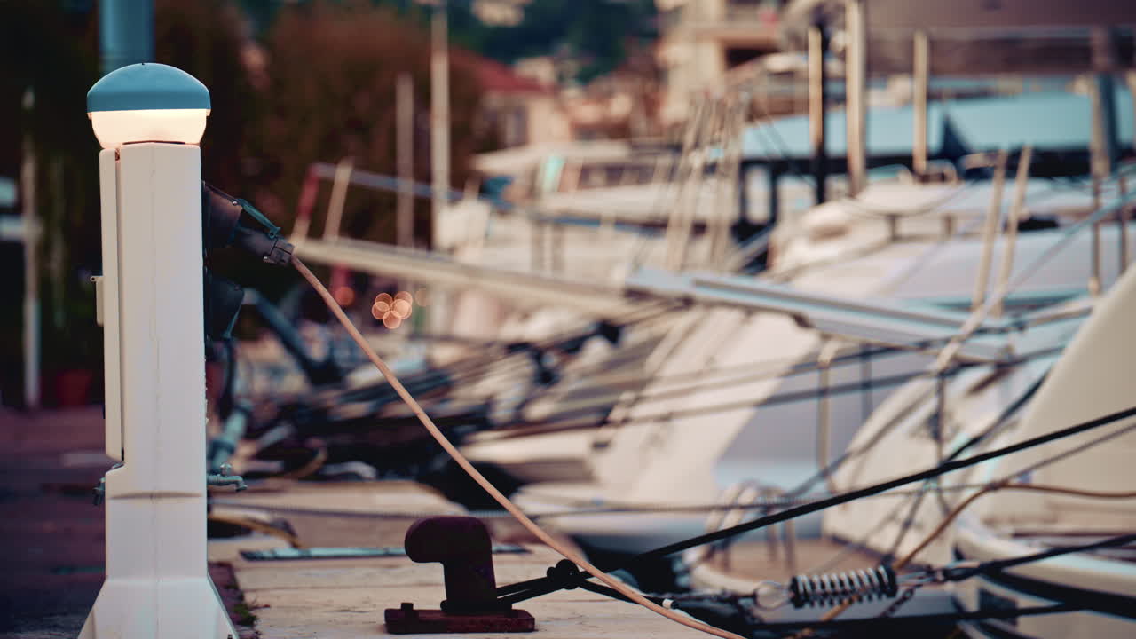 Close up of a white marina electrical pedestal glowing softly with cables running across the dock, and a rusted bollard sits near the edge