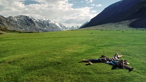 three attractive girls lying on green grass and having fun on a meadow sunny day and background of mountain