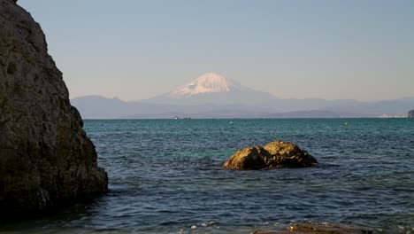 disparo de bajo ángulo en la playa con rocas y el monte fuji en la distancia