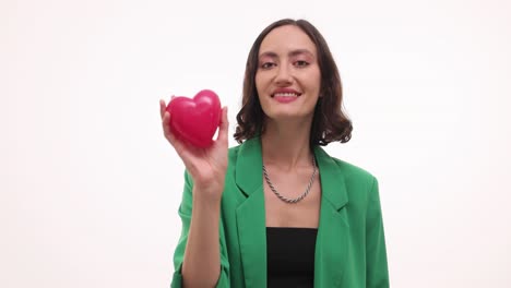 a smiling woman in a green blazer holds a pink heart