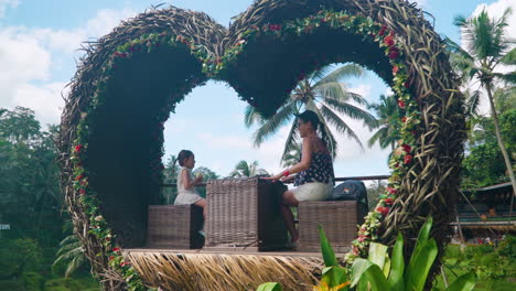 Asian-Woman-With-Daughter-In-Heart-shaped-Photo-Booth-At-Alas-Harum-Bali,-Indonesia