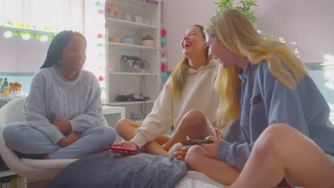 group of multi-cultural teenage girl friends with mobile phones hanging out in bedroom at home