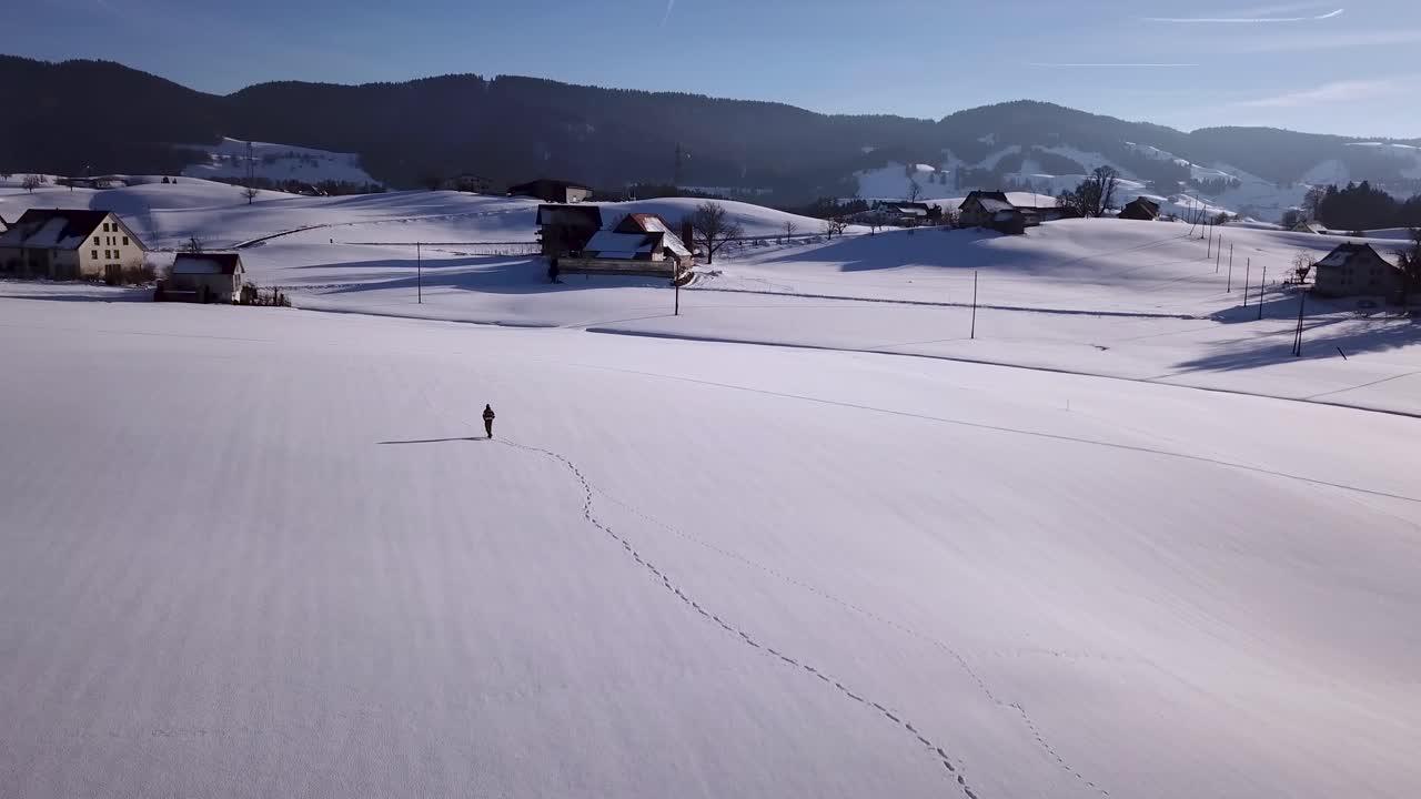 Un giovane uomo cammina in un vasto campo innevato, si ferma e si guarda intorno in Svizzera durante l'inverno