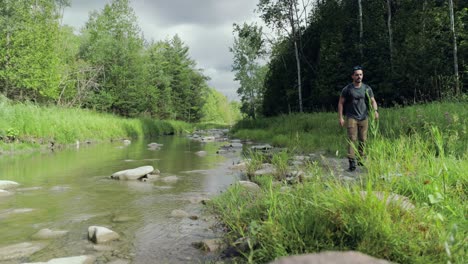 hiker wearing backpack explores lush river bank on cloudy summer day