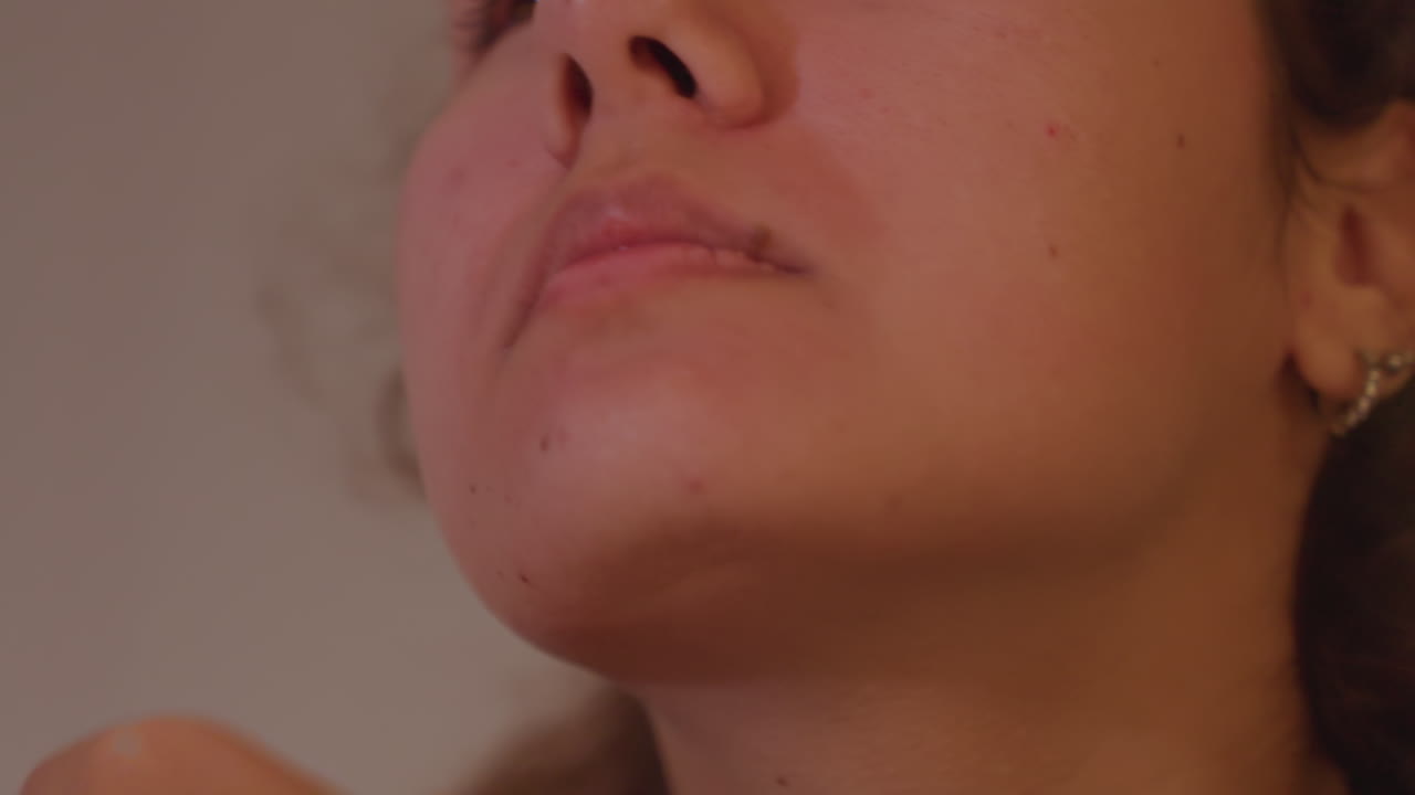 Primo piano del viso di una donna che mostra stanchezza ansiosa. Inquadrature strette catturano mento, bocca, mano che copre l'occhio. Respiro sottile, luce calda e soffusa, umore introspettivo, dettaglio autentico della cura della pelle, calma silenziosa.