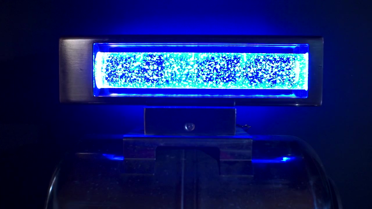 A futuristic cyber punk power-core device glows with intense blue light as shimmering particles and bubbling energy move inside its illuminated chamber.