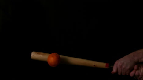 bate de béisbol golpeando una naranja en fondo negro