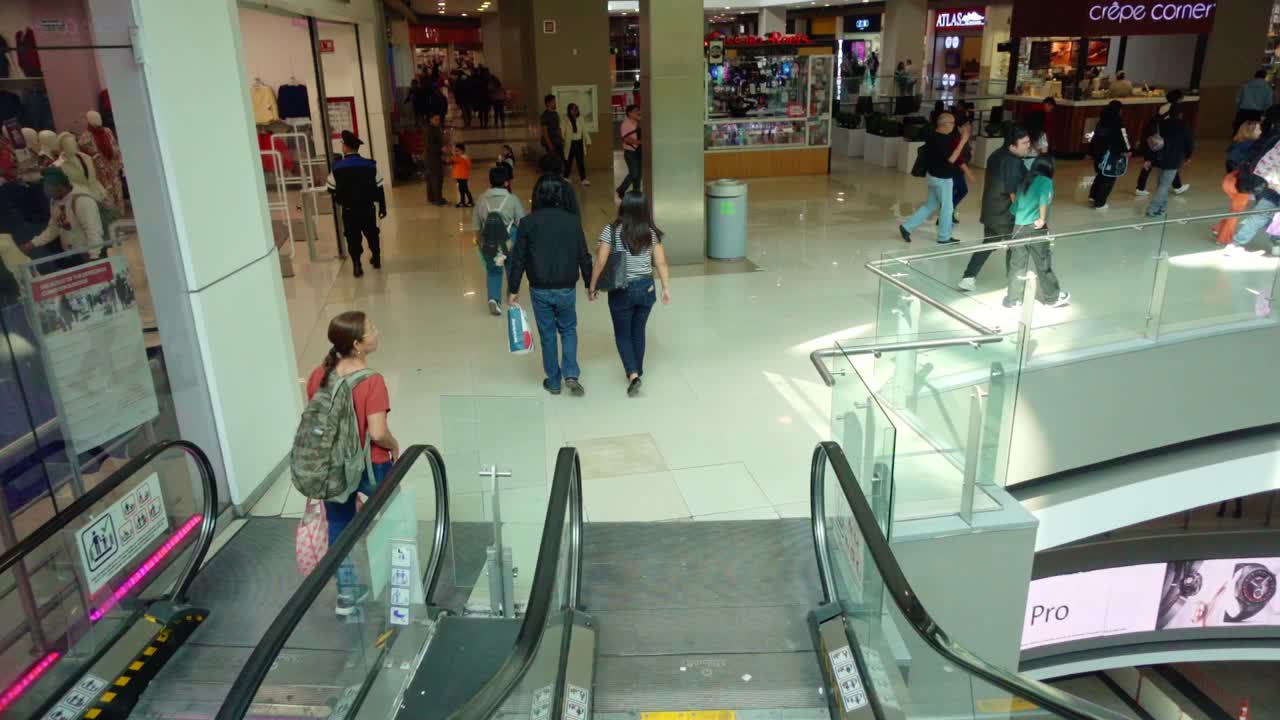 Shoppers move through a busy multi-level mall with escalators and various storefronts