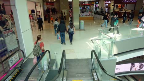 shoppers move through a busy multi-level mall with escalators and various storefronts