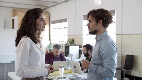 vista lateral de una mujer seria hablando con un colega confiado con gafas