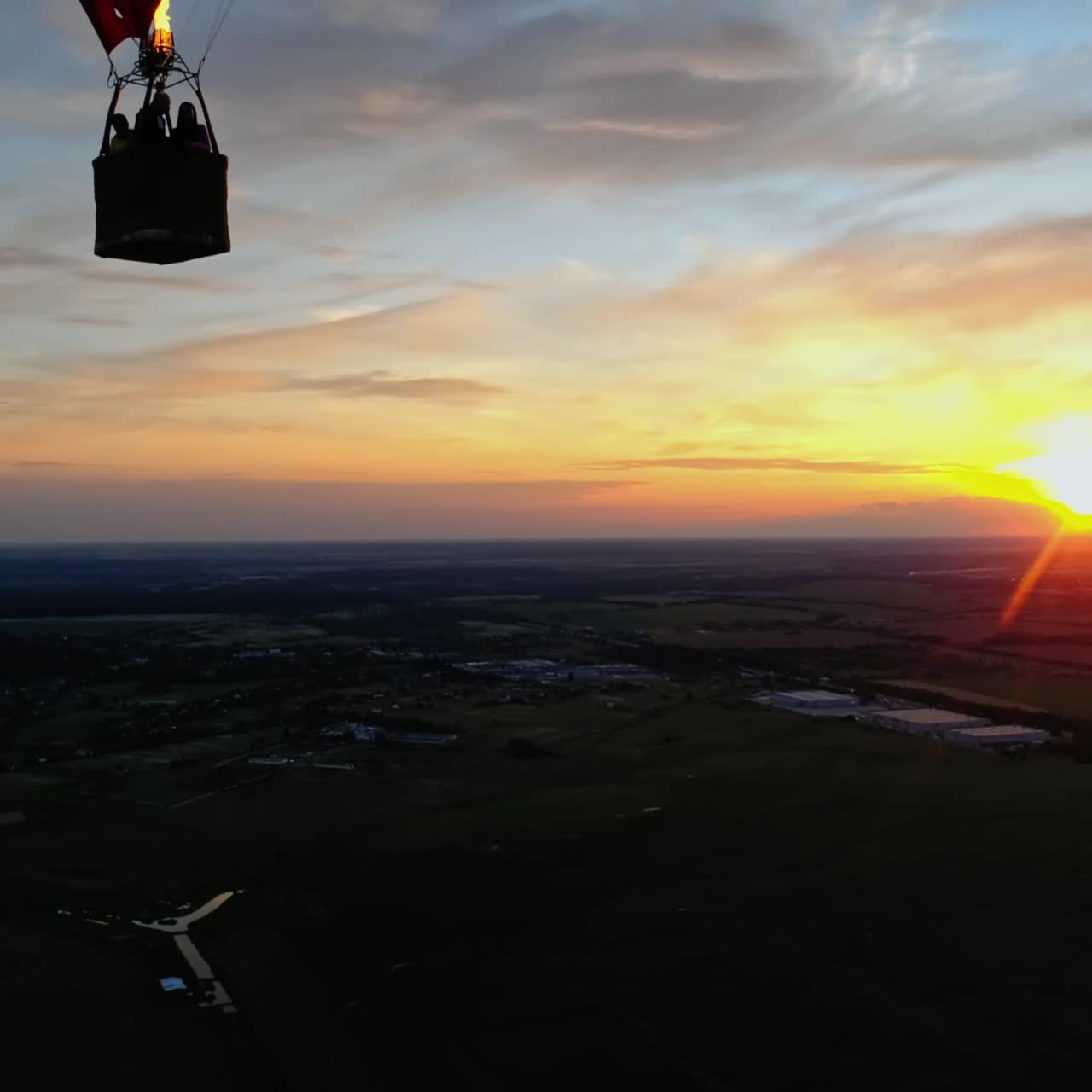 People travel in hot air balloon. Beautiful red aerostat in the form of a heart flying in the sky against orange sunset.