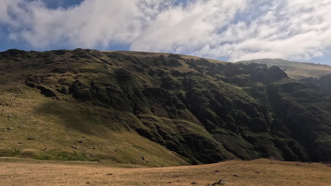 Clouds drift over green grassy rustic mountain ridge with copy space