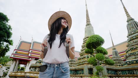 cheerful young asian woman traveling at wat pho temple in bangkok, thailand.