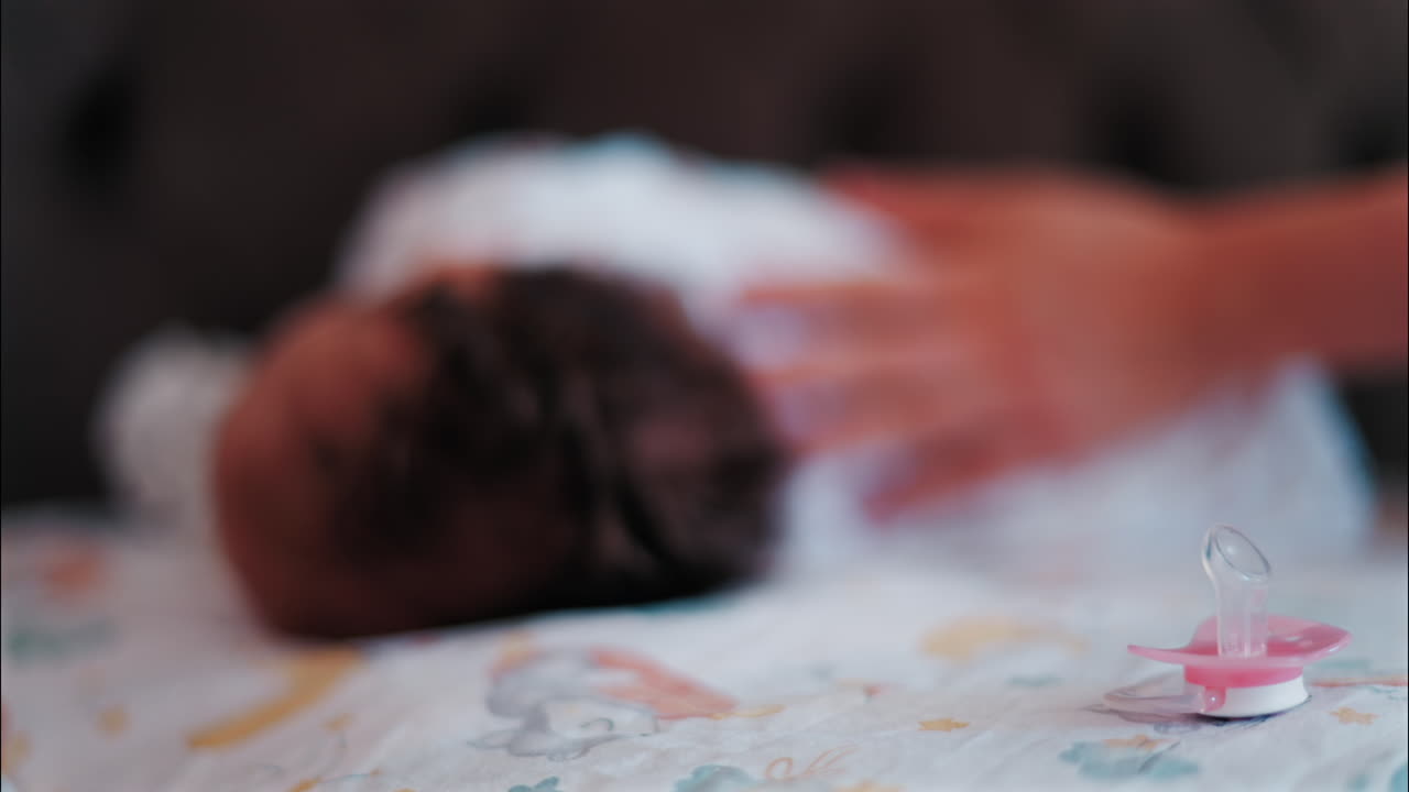 Close up of a pink pacifier with a baby lying down and sleeping peacefully in the background