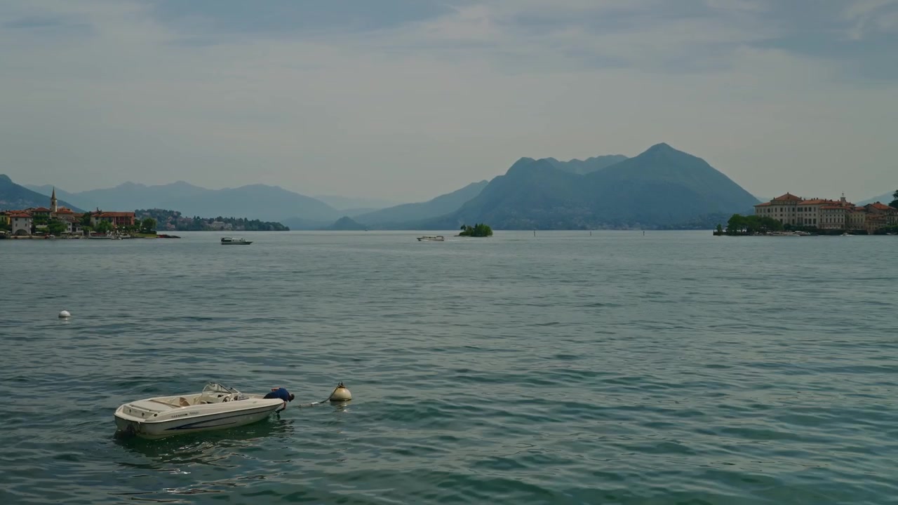 Vista perfetta da cartolina di un uomo in una barca che ondeggia dolcemente sul tranquillo Lago Maggiore con le Isole Borromee e maestose montagne alpine che creano una classica scena lacustre italiana