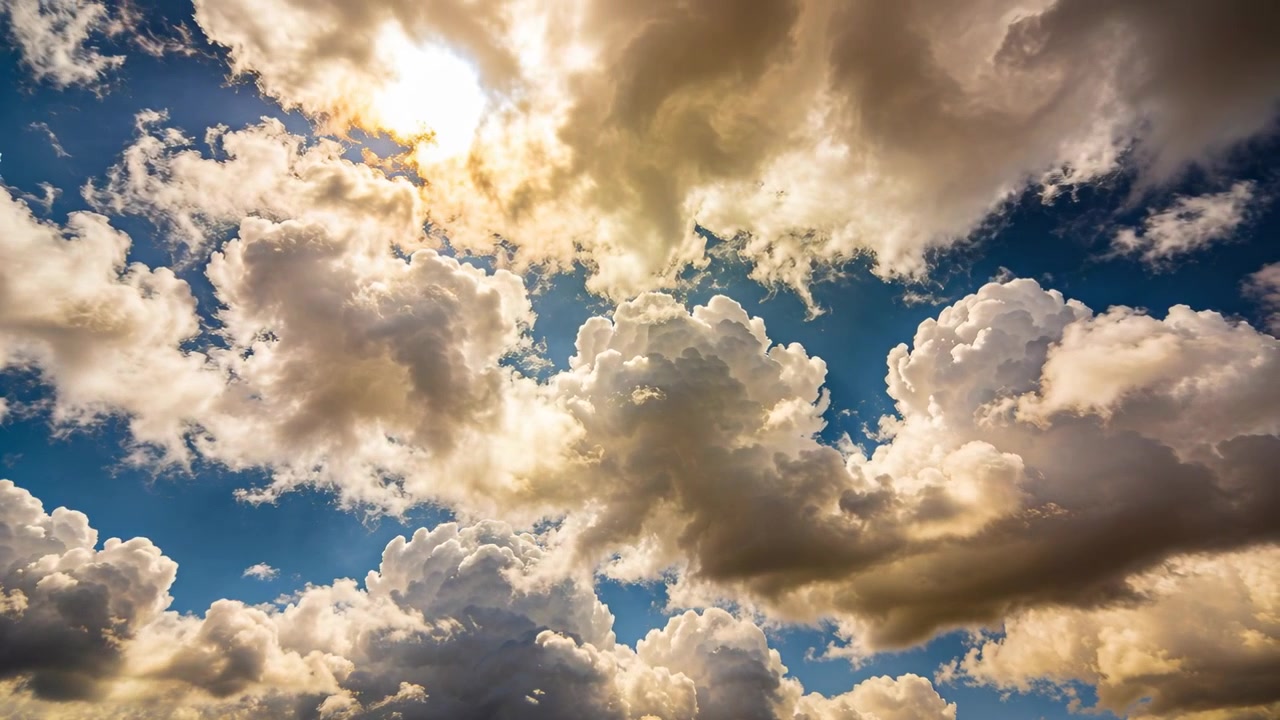 Grande ammasso di cumuli che si sposta mentre il sole fa capolino, muovendosi nel cielo blu, rivelando un'illuminazione di contorno.
