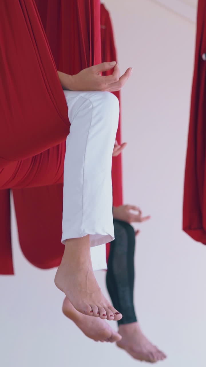 relaxed barefoot women legs sitting in fly yoga red hammocks holding fingers in mudra position low angle shot close view