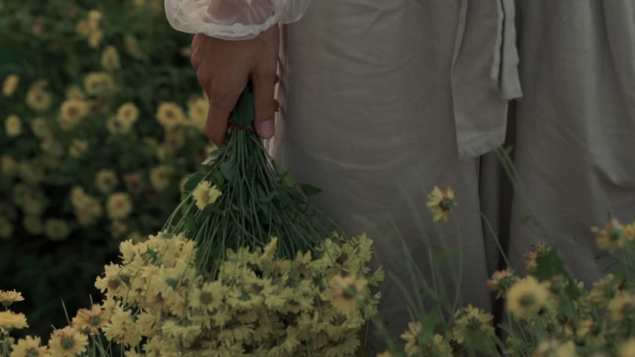 Close-up of a Hand Holding a Bouquet of Yellow Flowers in a Field