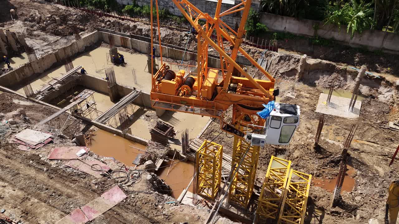 Aerial view of a construction site with a large crane and workers in muddy foundation pits