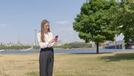 Mujer-Elegante-Comprobando-El-Smartphone-Con-La-Ciudad-De-Riga-En-Segundo-Plano.