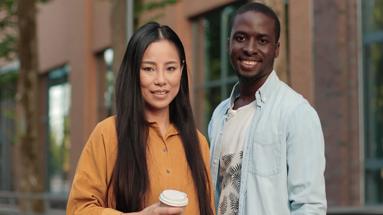 African american and asian students looking at the camera while standing near the university in a break