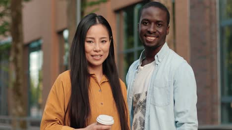 african american and asian students looking at the camera while standing near the university in a break