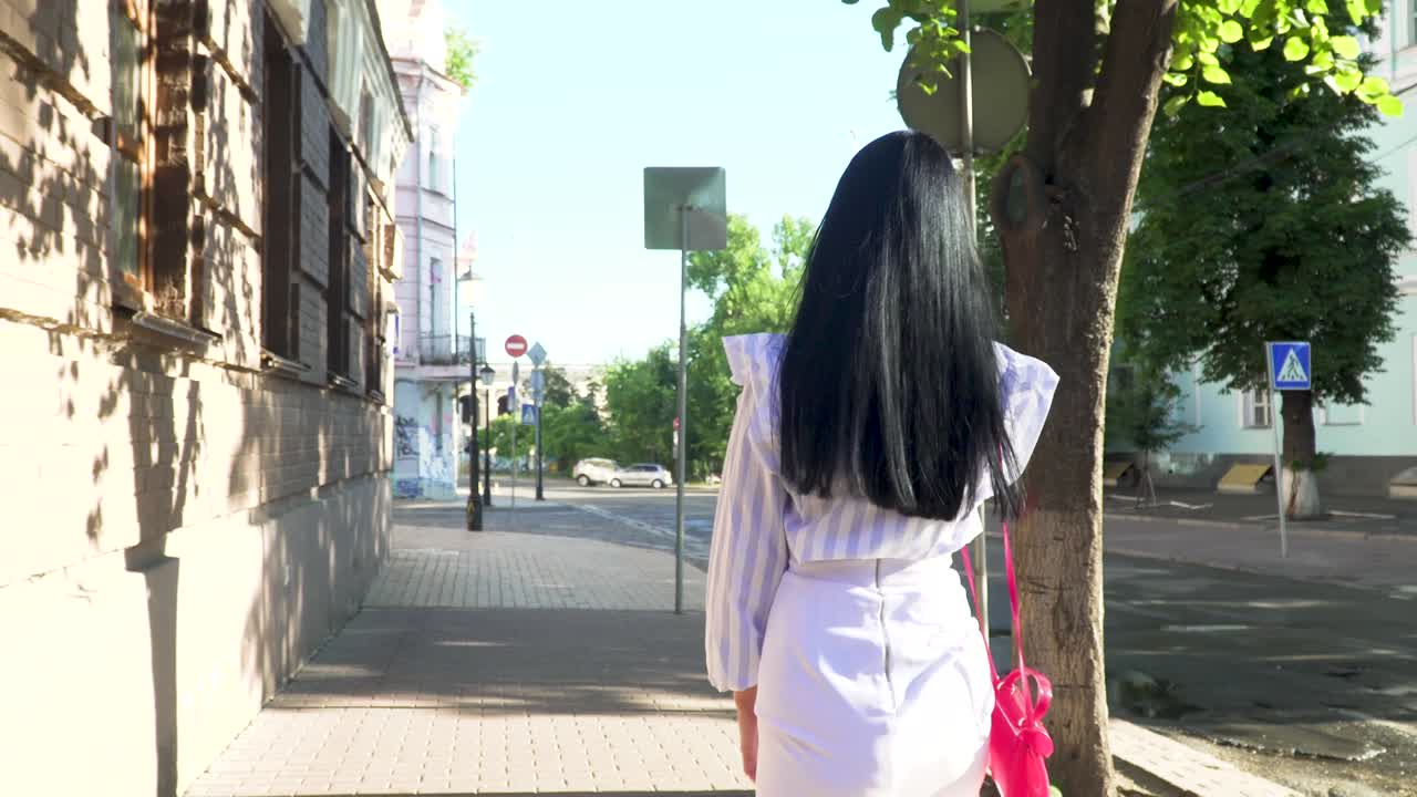 긴 머리카락을 가진 갈색 여성이 전화로 이야기하고 도시의 중심에서 고 있습니다.