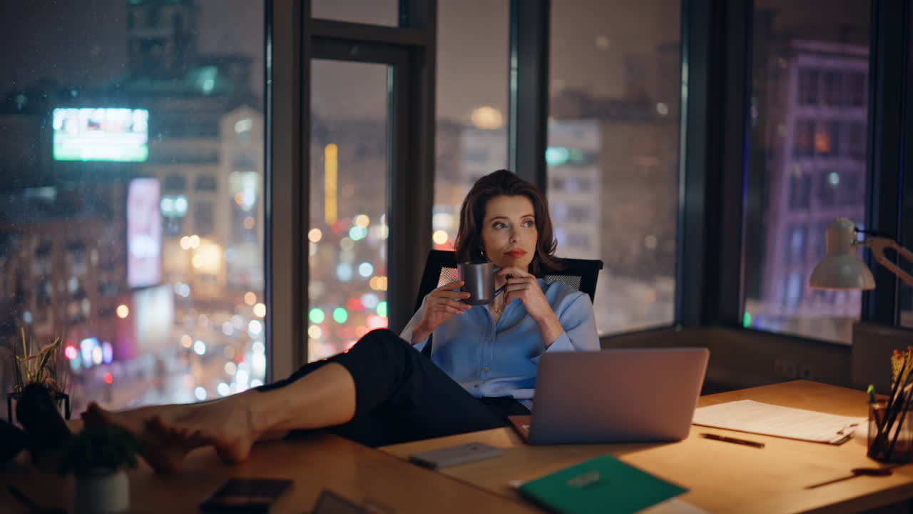 Relaxed overtime worker resting in night office putting bare feet on work desk
