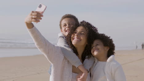 happy american mother and two children taking selfie while spending time at seashore