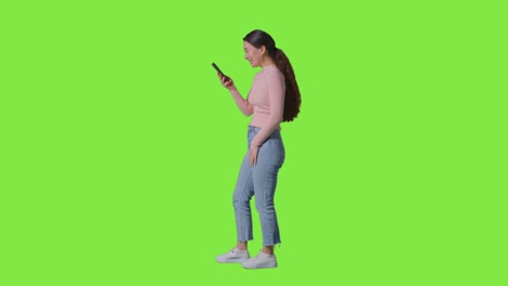 Ganzkörperprofil-Studioaufnahme-Einer-Lächelnden-Frau,-Die-Ihr-Mobiltelefon-Vor-Einem-Grünen-Bildschirm-Benutzt