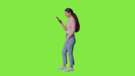 fotografía de estudio de perfil completo de una mujer sonriente usando un teléfono móvil contra una pantalla verde