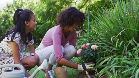 madre y hija afroamericanas felices, cuidando de las plantas al aire libre