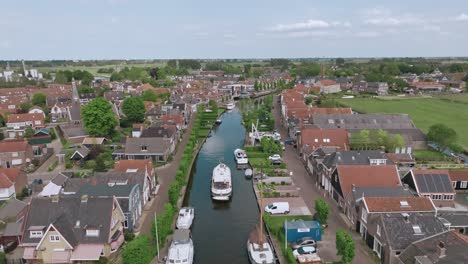 drone zooms in over a canal lined with boats and houses in netherlands on a sunny day with clear skies
