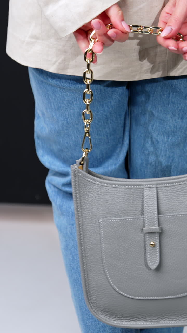 Beautiful grey leather bag with golden chain handle in female hands. Woman in jacket and jeans holding a modern handbag. Vertical video