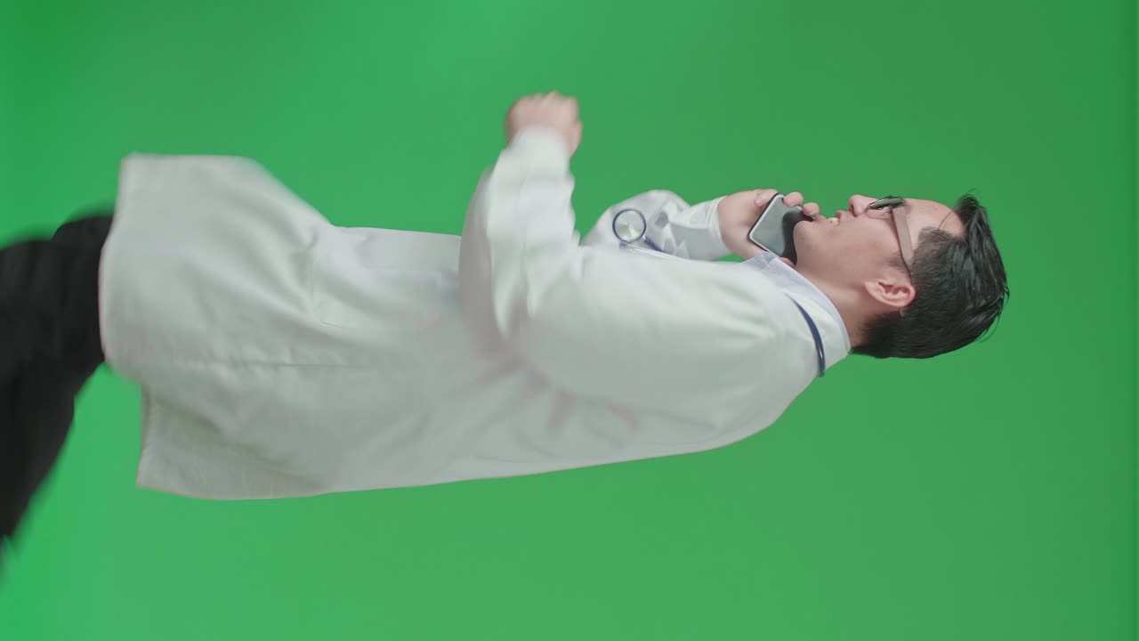 The Side View Of Asian Doctor With Stethoscope Wearing Glasses And White Coat Talking On Mobile Phone While Running On Green Screen Chroma Key.