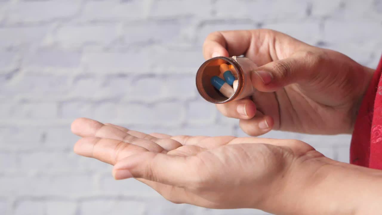 persona vertiendo pastillas de la botella en la mano