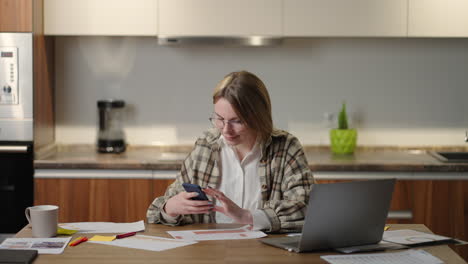 A-woman-at-home-with-a-mobile-phone-and-laptop-looks-and-smiles