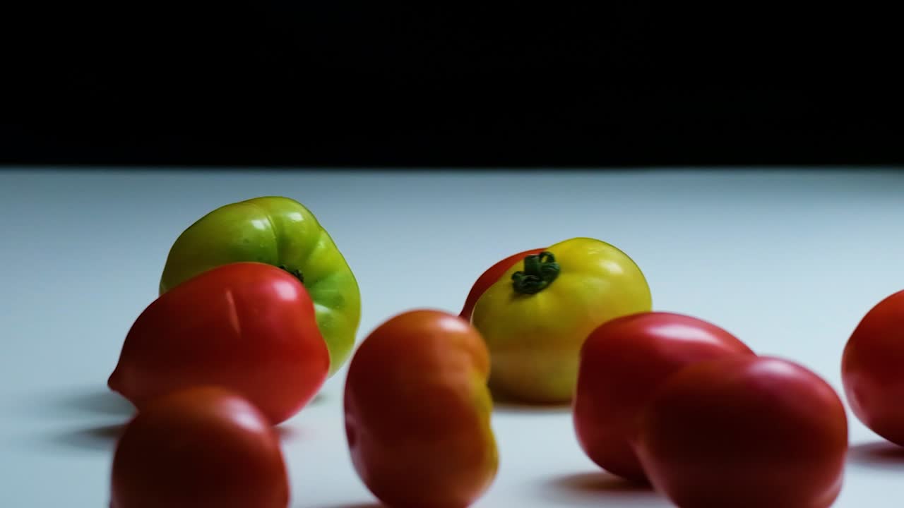 disparo inverso de un manojo de tomates de reliquia cayendo sobre una mesa de cocina blanca