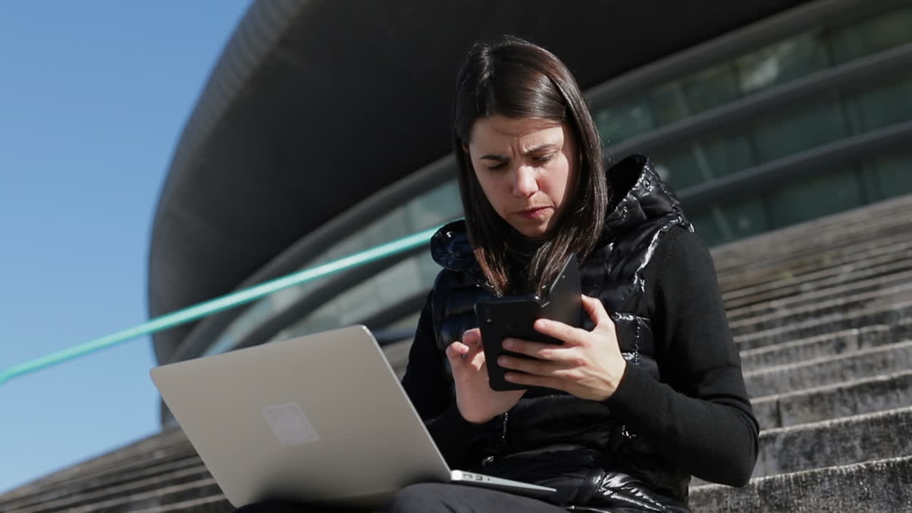 joven de cabello oscuro en un cálido chaleco negro sentada en las escaleras afuera