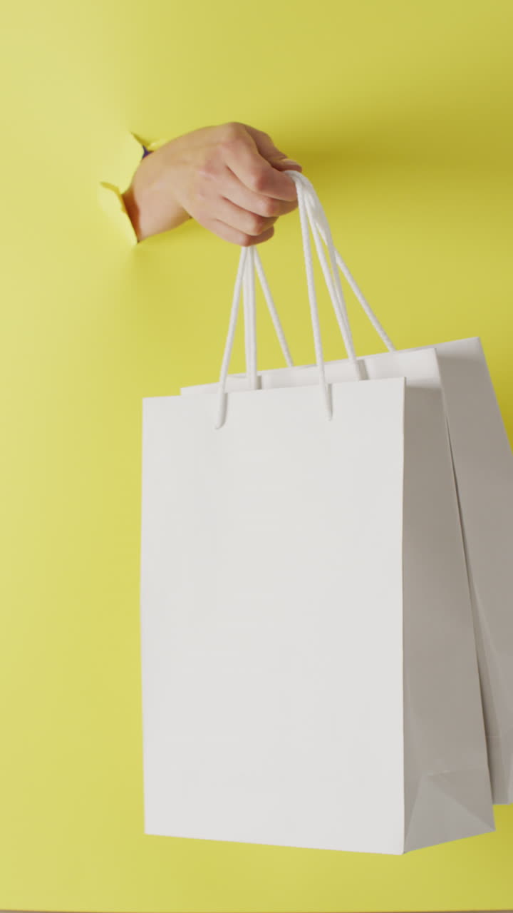 노란색 배경에 쇼핑 가방을 가진 손의 수직 비디오