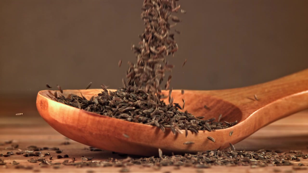 Caraway Seeds Pouring into a Wooden Spoon in Slow Motion